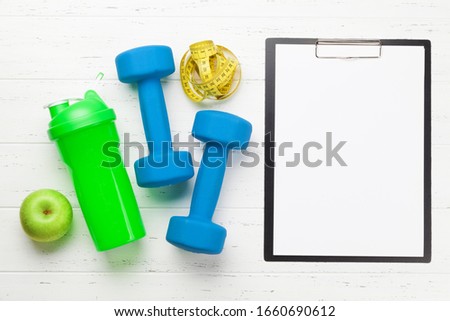 Fitness equipment and blank sheet for workout plan on a wooden background. Top view flat lay with copy space
