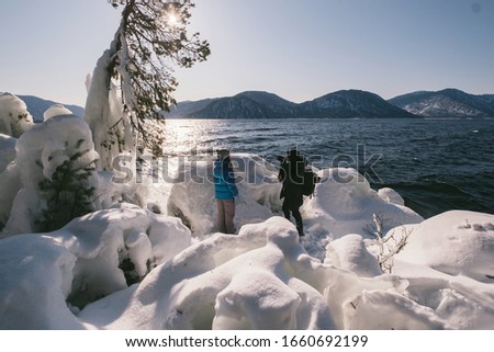 Photographer man takin photo of woman on winter snow covered  lake shore during sunny cold weather day