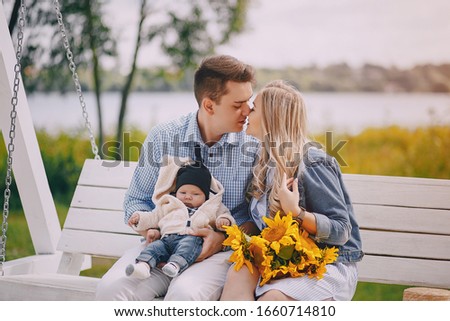 beautiful long-haired blonde with her handsome man and small newborn son sitting on the swing with sunflowers
