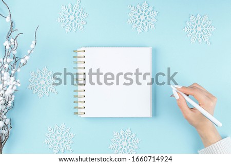 white notebook on a blue background with hand and gifts, holiday concept flat lay. new goals, plans and to do list top view.