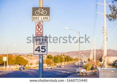 A silver metal pole with 3 signs indicating: bike lane, no parking anytime, and 45 MPH speed limit zone. Found on an undivided highway in Henderson, Nevada, USA.