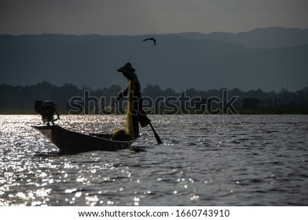 Traditional Intha leg-rowing fisherman with a cast net, illuminated by the setting sun, Inle Lake, Myanmar. 