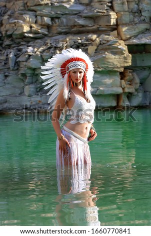 A young girl plays the part of a native American Indian. She
dresses up all in white wearing a white feathered headdress 
and is seen in a stone quarry lake.