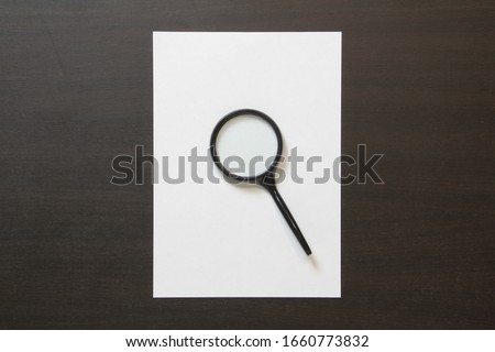 Template of white paper with magnefy on dark wenge color wooden background. Concept of searching, detecting and solving problems. Stock photo with empty space for text and design.