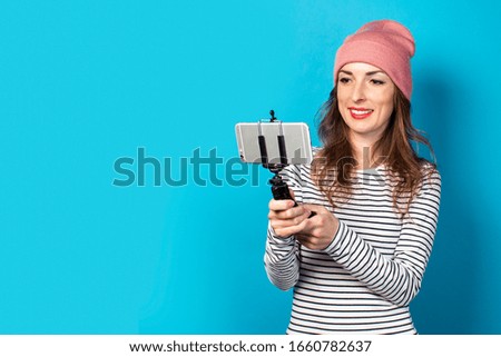 Young woman blogger takes pictures of himself on the phone on a blue background. Concept story, vlog, selfie, blog