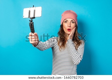 Young woman video blogger takes pictures of herself on the phone while broadcasting on a blue background. Concept story, vlog, selfie, blog