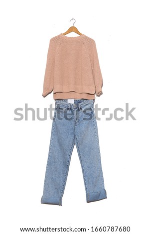 Beige sweater on hanging and blue jeans on white background

