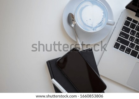 A coffee cup with milk during a break at work, Desk office and laptop, smartphone and notebook at office in the morning