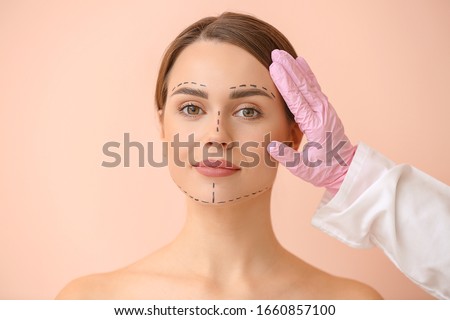Plastic surgeon touching face of young woman on color background Royalty-Free Stock Photo #1660857100