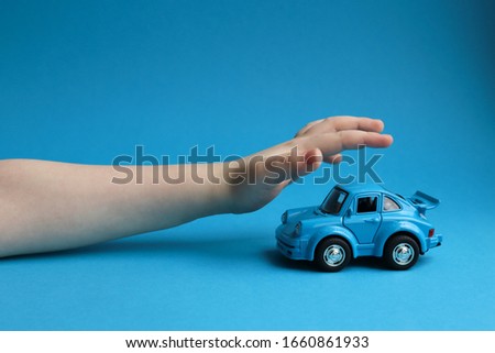 Blue toy car on a blue background and a children's hand that wants to take it Royalty-Free Stock Photo #1660861933