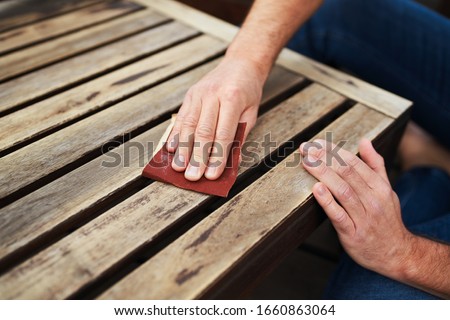 Man sitting outdoors on terrace and sanding wooden furniture Royalty-Free Stock Photo #1660863064