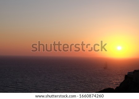 Sunset view with a sailing ship entering an orange mist, from a cliff