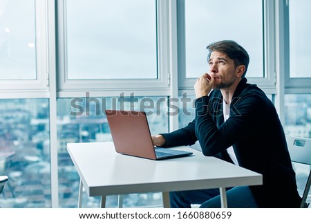 A man sits in front of an open laptop in the office near the window