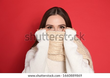 Young woman wearing warm sweater and scarf on red background. Winter season