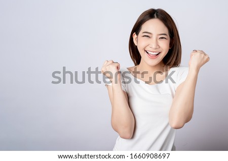 Asian pretty woman in white t-shirt and white pants pretending glad happy face with copy space on white background. Information telling, shopping promotion, announcement, selling support concept. Royalty-Free Stock Photo #1660908697
