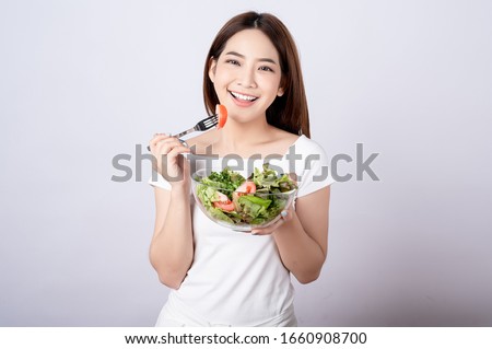 Beautiful young asian eating salad with big smile happy beaming face in seamless white  isolated background. Diet healthy concept. Her face and skin are healthy, fresh, bright and youthful.
 Royalty-Free Stock Photo #1660908700