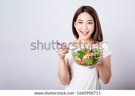 Beautiful young asian eating salad with big smile happy beaming face in seamless white  isolated background. Diet healthy concept. Her face and skin are healthy, fresh, bright and youthful.
 Royalty-Free Stock Photo #1660908715