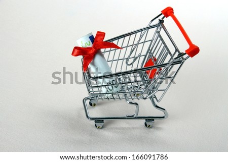 Mini shopping cart with hundred euro and red ribbon, top view
