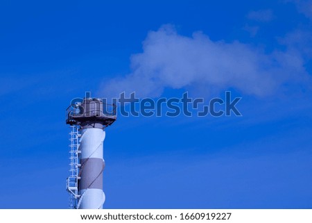 The steaming tube or pipe of the plant, factory or thermal power station on the background of clear blue sky