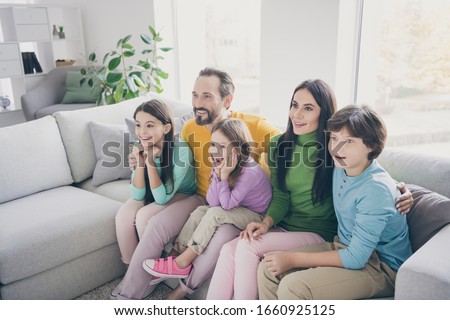 Excited crazy energetic family dad daddy mom mommy three small preteen kids schoolboy schoolgirl sit comfort couch watch incredible tv series amazed in house room