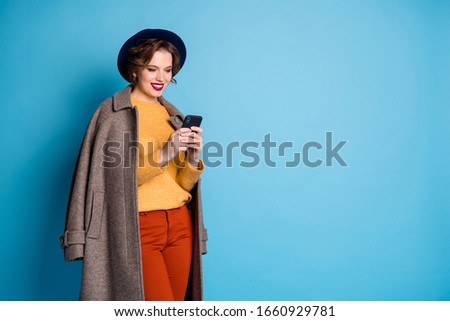 Photo of pretty lady walk down street traveler search telephone nearest shopping center wear casual long grey coat pullover trousers hat shoes isolated blue color background