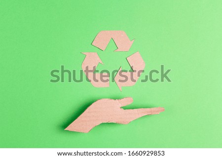 Arrows recycle eco symbol on cardboard hand silhouette on green background. Recycled cycle sign.