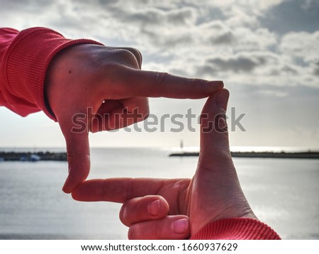 Fingers gesturing picture frame on sunrise seaside. Sunlight on beach. Sunset at the sea. Hand-made gesture in love concept, female  wrist
