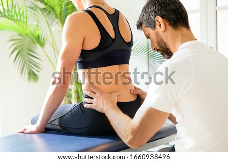 Osteopath doing a lumbosacral evaluation on a seated woman manipulating the muscles and spine of the lumbar and sacral regions of her lower back with his hands in close up Royalty-Free Stock Photo #1660938496