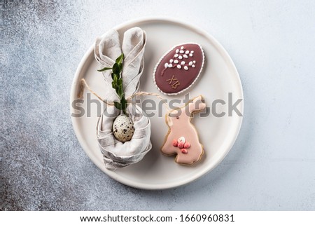 Table setting for the holiday of Easter. The photo shows white dishes, serving mat, Easter egg in a napkin. Napkin draped under rabbit ears.