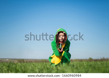 Funny girl in pajamas costume dragon sitting on the lawn, on the horizon and calls to his