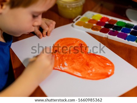 A child draws a heart in watercolor on paper. Boy, leisure, drawing.