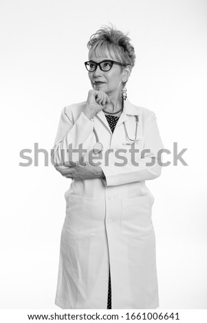 Studio shot of senior Asian woman doctor standing and thinking while wearing eyeglasses against white background