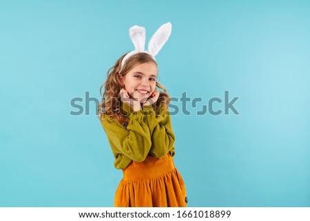 Photo of amusing blonde girl in toy rabbit ears smiling at camera isolated over blue background