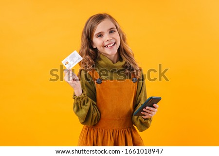 Photo of joyful beautiful girl holding cellphone and credit card isolated over blue background