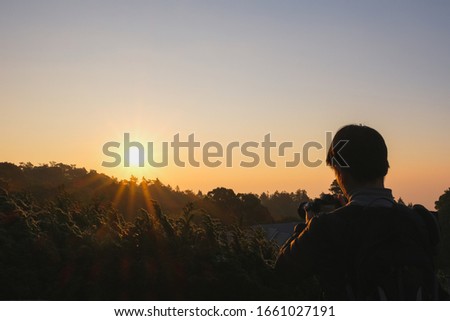 A photographer man standing on the top of the hill At sunrise,Light from the sun Yellow warm Sunset dawn Silhouette Chiang Mai Thailand, ASIA. tourist