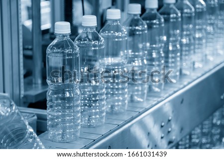 The PET bottles in the rail on the conveyor belt for filling process in the drinking water factory. The drinking water factory production process by automatic filling machine in the plant.  Royalty-Free Stock Photo #1661031439
