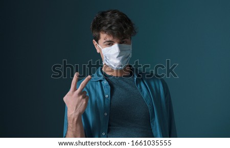 Confident millennial posing with a face mask and making a V sign gesture, virus spread and disease prevention concept