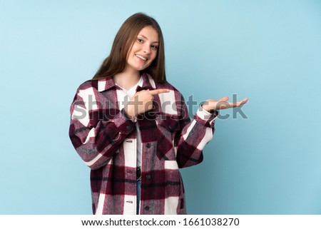 Teenager caucasian girl isolated on blue background holding copyspace imaginary on the palm to insert an ad