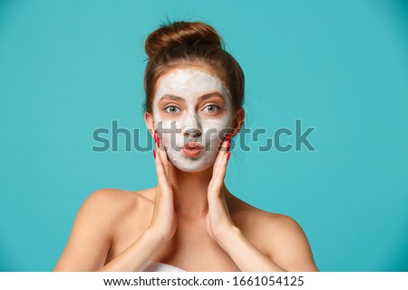Young woman with towel wrapped around her body applying clay face mask and having fun. Daily morning routine - facial cleaning, skin care, peeling, moisturising and beauty treatment concept Royalty-Free Stock Photo #1661054125