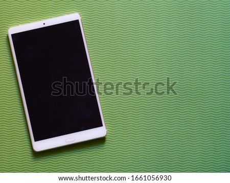 Blank for lettering call to action. The tablet screen lying on a flat green table background. Use in mobile marketing, advertising communication technologies, mobile services. Top wiew.