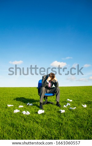 Disappointed businessman sitting with head in hands outdoors with paper balls littering the field around him