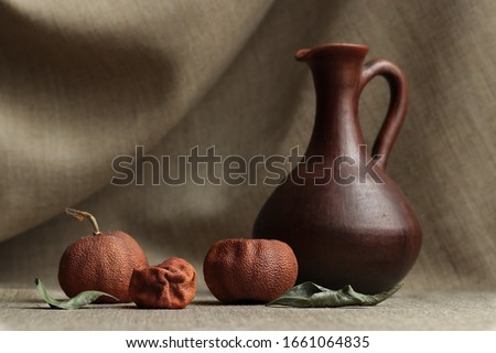 Still life of dried tangerines and leaves with a clay brown jug on a natural material Royalty-Free Stock Photo #1661064835