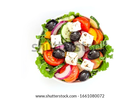 Greek salad with tomato and fresh vegetables in white bowl on white background. Top view