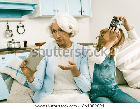 Conflict Of Generations Grandmother With Her Granddaughter Cannot Understand Each Other's Gadgets Granny Holding Mobile Or Smart Phone Making Photos
