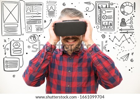 Hand drawn UI or UX pictures with excited guy holding VR headset. Studio shot of young man testing virtual reality glasses. Technology concept