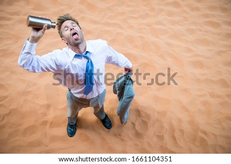 Thirsty businessman standing on red sand desert pouring an empty water bottle over his tongue Royalty-Free Stock Photo #1661104351
