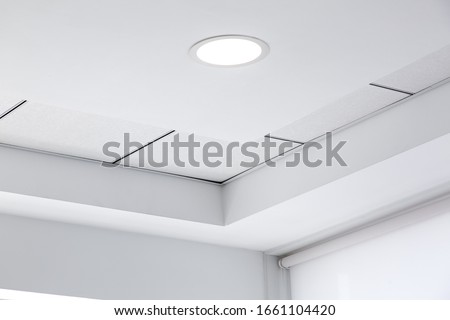 multi-level ceiling with three-dimensional protrusions and a suspended tiled ceiling with a built-in round led light in the corner of the room, close up details. Royalty-Free Stock Photo #1661104420