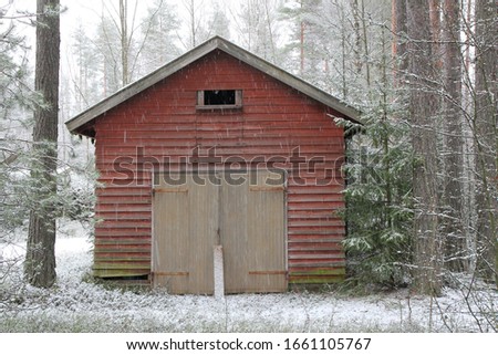 Red garage with a green door in the snow. A board to keep the doors closed.