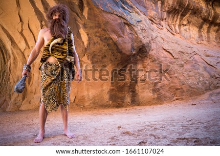 Caveman standing outdoors holding his club in an empty cave  Royalty-Free Stock Photo #1661107024