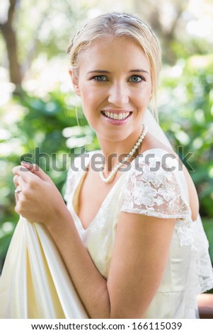Smiling blonde bride holding her dress looking at camera in the countryside